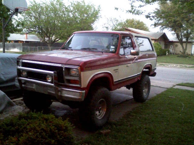 1986 Ford Bronco with off-road tires and brush guard parked on a driveway.