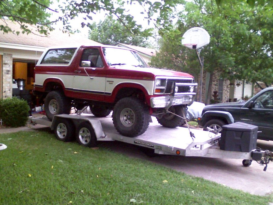 Lifted red and white Ford Bronco loaded on an aluminum car trailer in a driveway