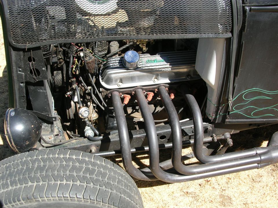 V8 engine with chrome Edelbrock valve cover and black lake headers on a black rat rod