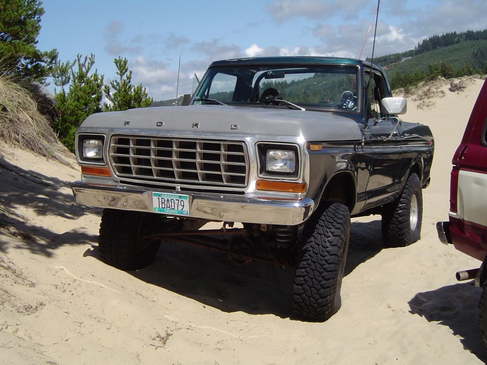 Silver and black classic Ford pickup truck parked on sand, front view