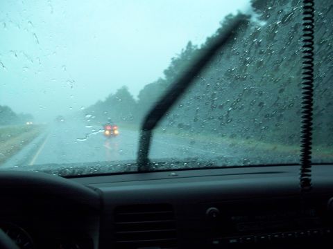 1996 Ford Bronco - View from inside a vehicle driving on a highway during a rainstorm, with the windshield wipers active. The dashboard and part of the steeri…
