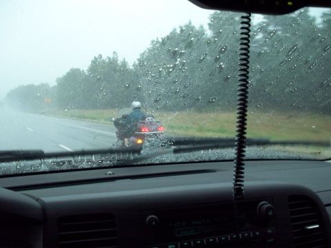 1996 Ford Bronco - View from inside a vehicle looking out at a motorcycle rider on a wet road in the rain. The motorcycle has a large red taillight and a whit…