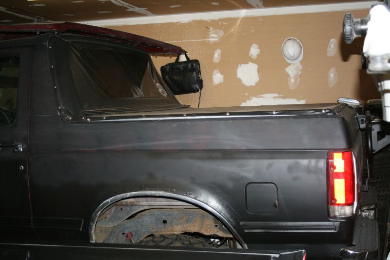 Side of a black SUV body shell with rear quarter and taillight in a garage