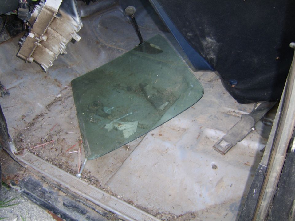 Removed automotive door glass lying on a vehicle floor pan