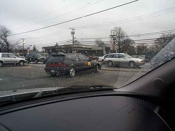 Black Civic hatchback with R decal seen across wet lot through car windshield