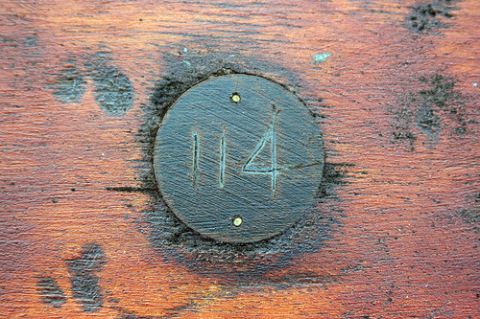 1992 Ford Bronco - A circular dark wooden plaque with the number "114" carved into it is affixed to a weathered wooden surface.
