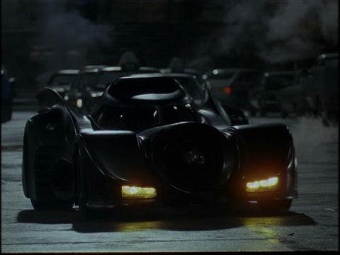 1988 Mercury Grand Marquis - The front view of a black custom Batmobile-style car with yellow headlights is shown in a dimly lit, smoky outdoor setting.