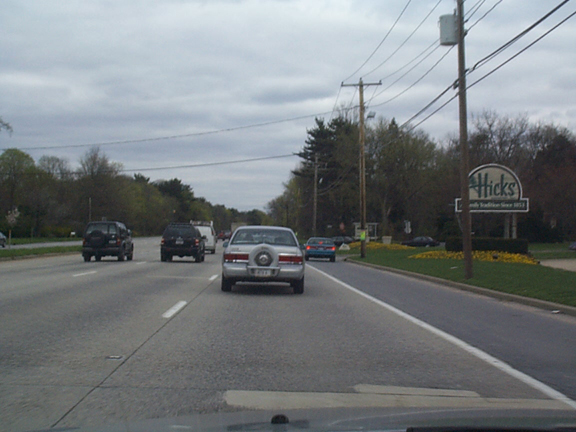 Silver sedan with continental kit spare cover ahead on highway past Hicks sign