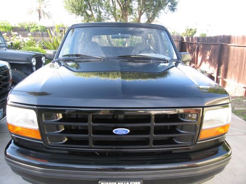1986 Ford Bronco - Front-end view of a black 1992-1996 Ford F-150 pickup with murdered-out grille and Ford oval, parked in a fenced backyard.