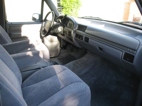 1986 Ford Bronco - The interior of a Ford Bronco shows the driver's side seat, dashboard, and steering wheel. The seats are upholstered in a gray fabric with…