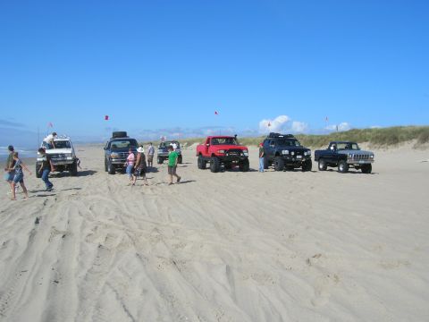 1996 Ford Bronco - Several off-road vehicles are parked on a sandy beach under a clear blue sky. People are standing around the vehicles, some interacting wit…