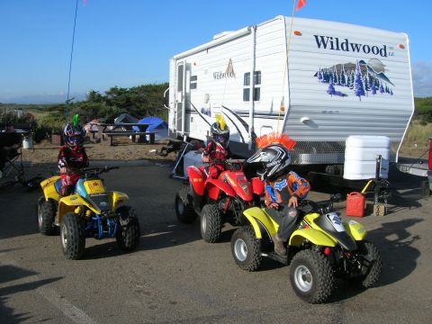 1996 Ford Bronco - Three children in riding gear sit on youth ATVs parked in front of a Wildwood RV. The ATVs are yellow and red, and the RV is white with blu…