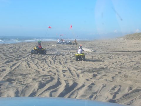 1996 Ford Bronco - A group of people ride ATVs on a sandy beach with the ocean in the background. One ATV in the foreground is yellow and ridden by a person w…