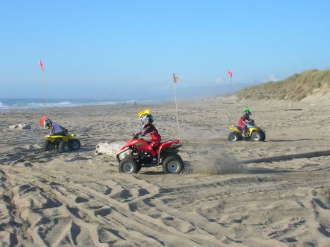 1996 Ford Bronco - Three children ride ATVs on a sandy beach with the ocean in the background. The child in the middle is kicking up sand as they ride.
