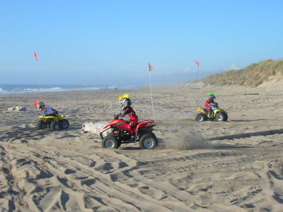 Children riding ATVs on a sandy beach.