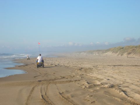 1996 Ford Bronco - Two people ride ATVs on a sandy beach near the ocean, with dunes in the background.