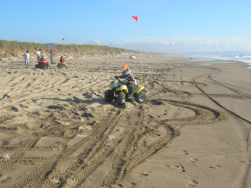 Yellow ATV on a sandy beach with tire tracks and people in the background.