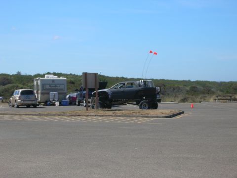 1996 Ford Bronco - A lifted black pickup truck with orange flags on poles is parked in a paved lot next to a trailer and a silver SUV.