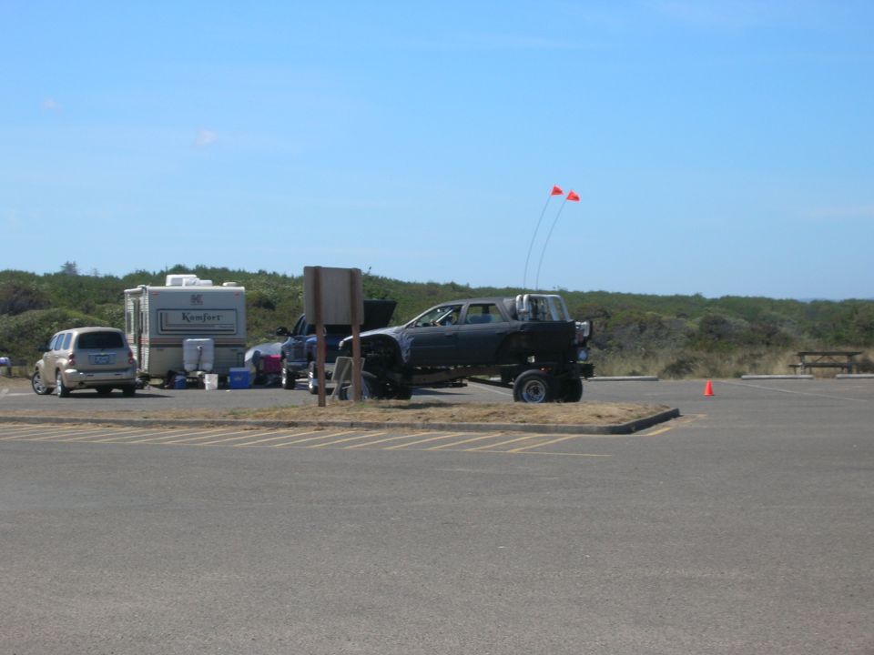 Lifted black pickup truck with orange flags, parked in a lot with a trailer and SUV.