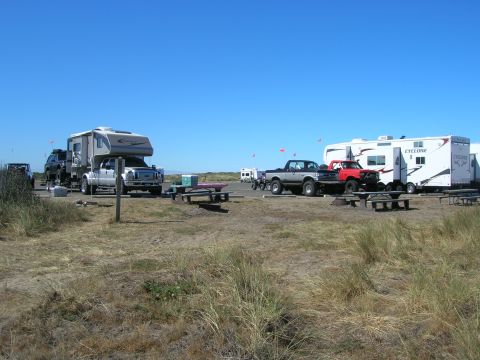 1996 Ford Bronco - A large white and gray truck camper is parked on a sandy lot next to a black SUV. Several other RVs and trucks are parked in the background…
