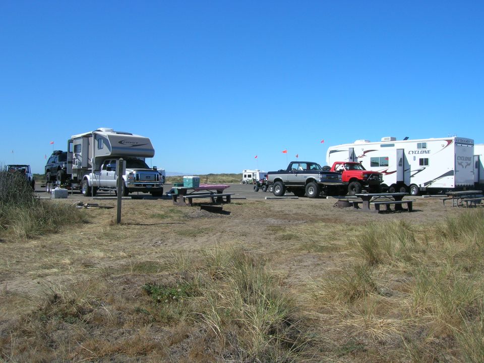 Truck camper and SUV parked on sand with RVs in background