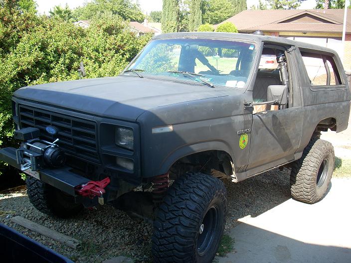 Matte black 1980s Ford Bronco with winch and large tires.
