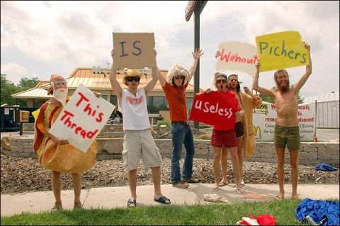 1988 Mercury Grand Marquis - A group of people are holding signs in front of a McDonald's restaurant. One person is wearing a hot dog costume.