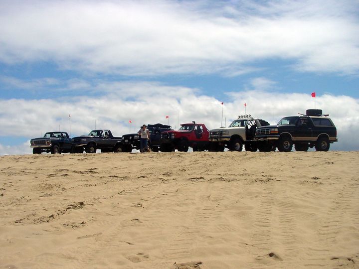 Several off-road trucks and SUVs parked on a sand dune.