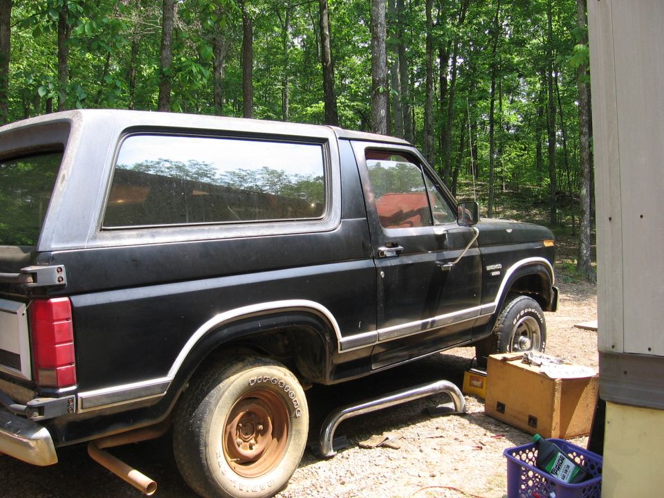 Black Ford Bronco parked outdoors with wooded background.