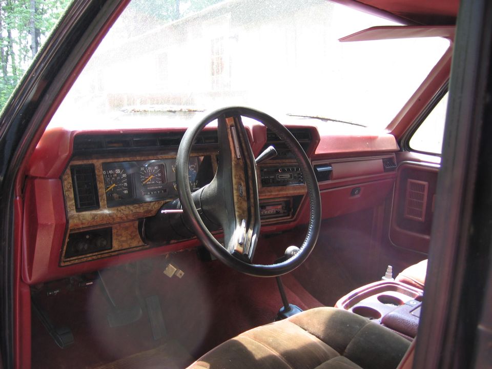 Red interior of a Ford Bronco with woodgrain dash trim, black steering wheel, and brown cloth seats