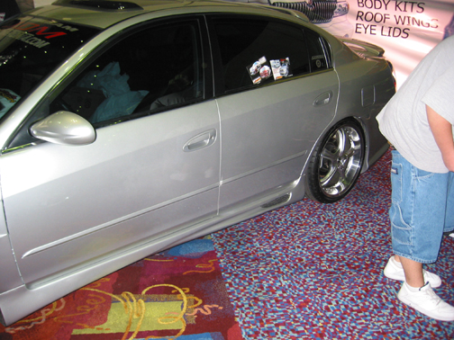 Lowered silver Nissan Altima side view with skirts and chrome lip wheels at show