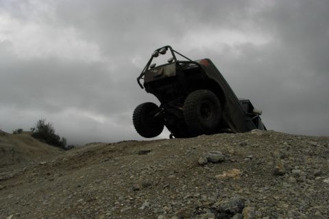 1991 Ford Bronco - Off-road vehicle on its side on a dirt hill with a cloudy sky overhead.