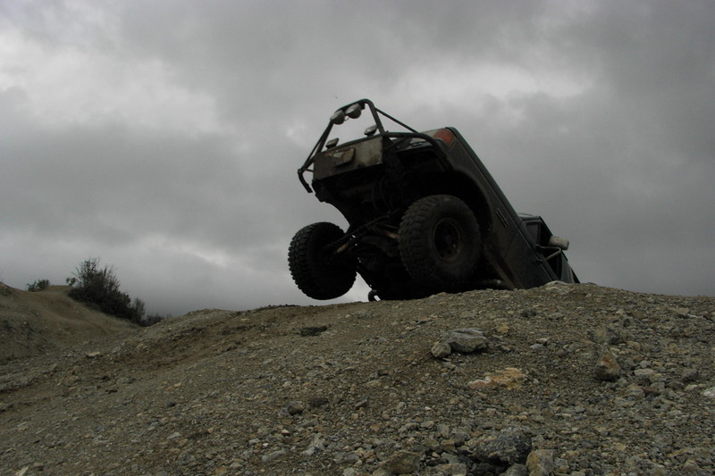 Off-road vehicle tipped onto its side on a rocky incline under a cloudy sky