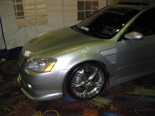 Front corner of silver Nissan Altima showing body kit, fog lights and chrome wheel