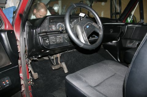 1989 Ford Bronco - The interior of a red vehicle, with a focus on the dashboard and driver's seat area.