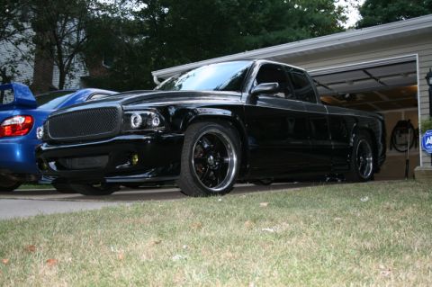 1989 Ford Bronco - Customized black pickup truck with aftermarket wheels and headlights sits in a driveway.
