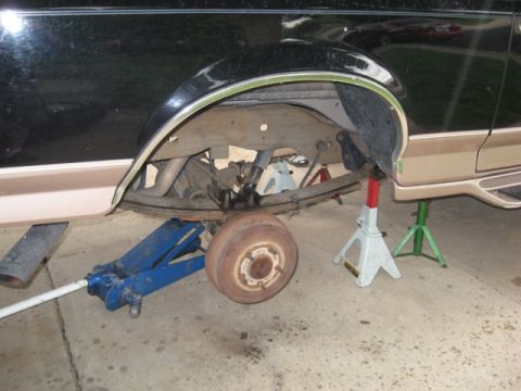 1996 Ford Bronco - Rear suspension of a dark-colored SUV is visible, supported by jack stands with the wheel removed.