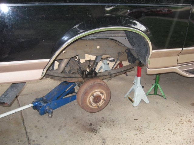 Black and tan SUV rear axle on jack stands, missing wheel