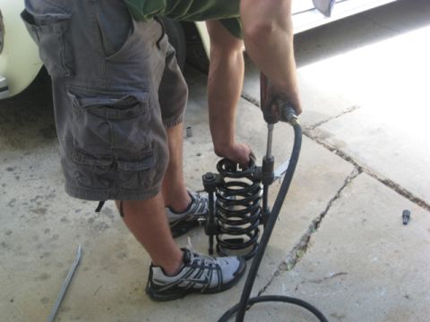 1996 Ford Bronco - A person is using a spring compressor tool to compress a coil spring, likely for vehicle maintenance.