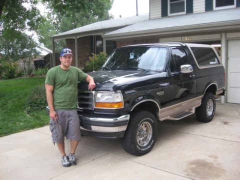 1996 Ford Bronco - A man stands next to a black 1996 Ford Bronco in front of a suburban house.