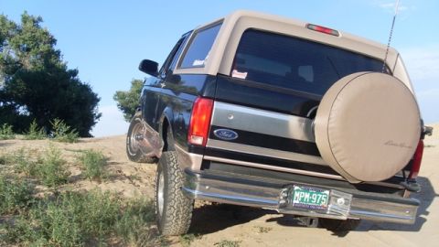 1996 Ford Bronco - 1996 Ford Bronco parked on a dirt hill, showing its rear profile and spare tire.