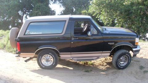 1996 Ford Bronco - This Ford Bronco is parked on a dirt road with trees in the background.