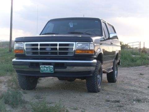 1996 Ford Bronco - A black 1996 Ford Bronco is parked on a dirt road with a fence and grassy field in the background.