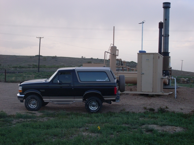 Black 1996 Ford Bronco parked on a dirt road next to industrial equipment