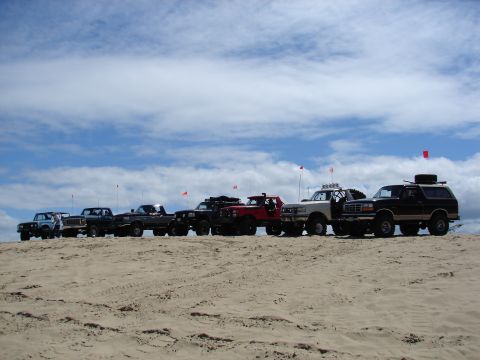 1996 Ford Bronco - Several Ford trucks and SUVs are lined up on a sandy dune with red flags visible.