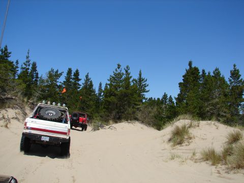 1996 Ford Bronco - Two off-road vehicles navigate sand dunes under a clear blue sky.