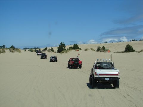 1996 Ford Bronco - A convoy of off-road vehicles traverses a vast sandy terrain on a clear day.