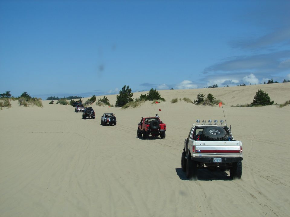 Several off-road vehicles driving in a line on a sandy dune landscape under a blue sky