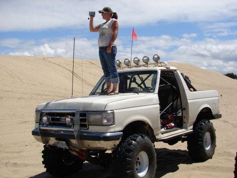 1996 Ford Bronco - Modified 1996 Ford Bronco with roll cage and off-road tires parked on sand dunes.