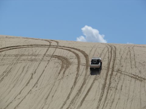 1996 Ford Bronco - A 1996 Ford Bronco navigates a sandy incline, leaving behind a trail of tire tracks under a blue sky.